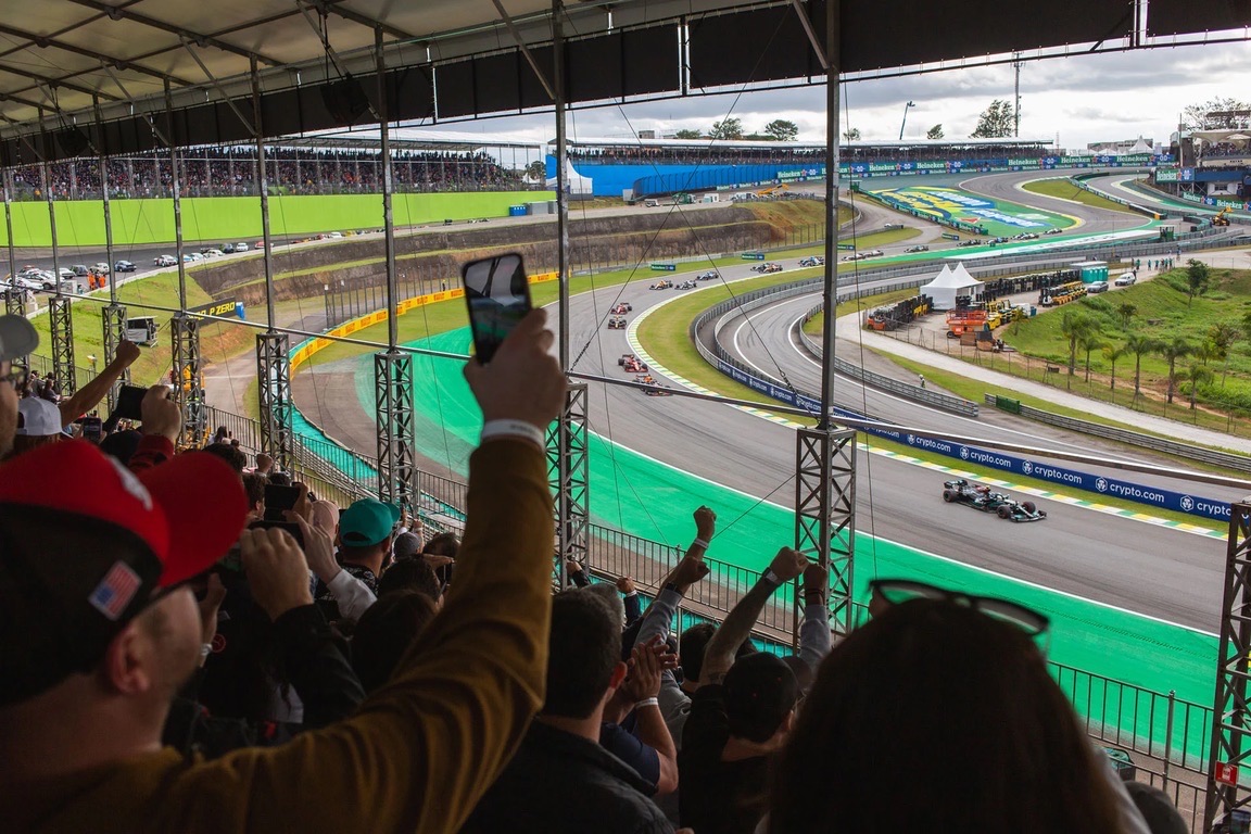 Autos de Fórmula 1 pasando por la curva de Interlagos, vistos desde una tribuna cubierta con el público celebrando