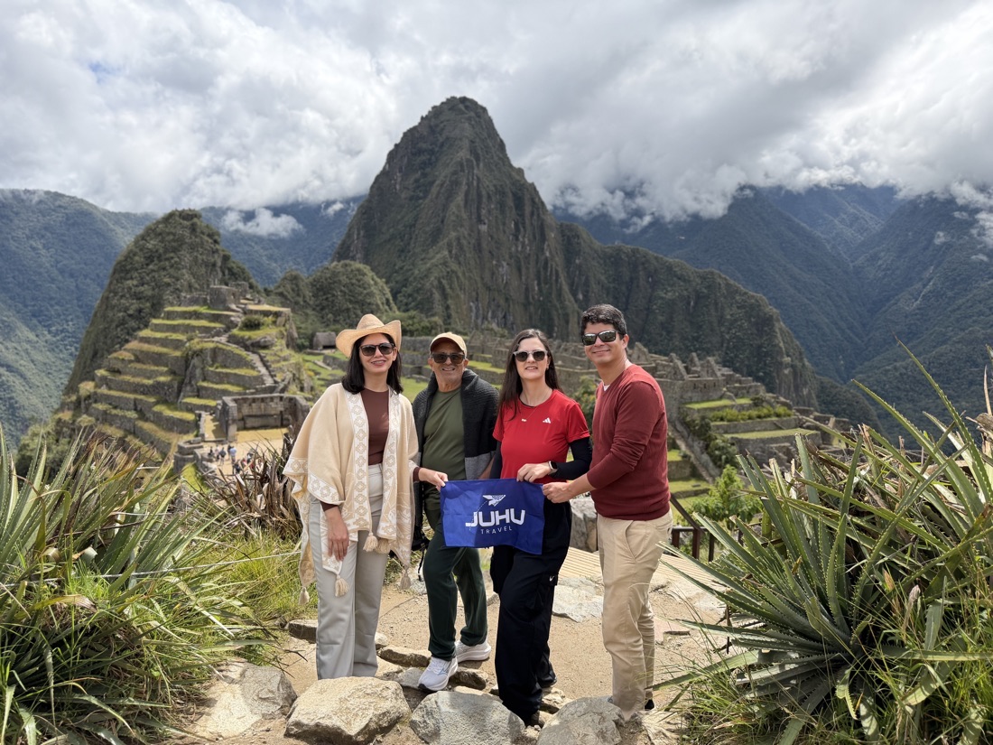 Bianca y Victor con viajeros de JUHU Travel en Machu Picchu, sosteniendo una bandera de la agencia