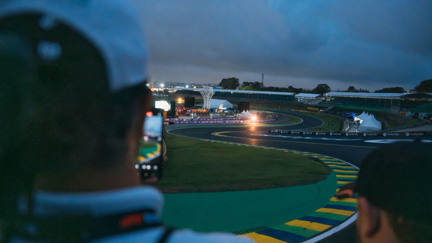 Recorrido guiado por la pista de Interlagos al atardecer: una curva del circuito vista desde el borde del asfalto, con un visitante sacando una foto con el celular