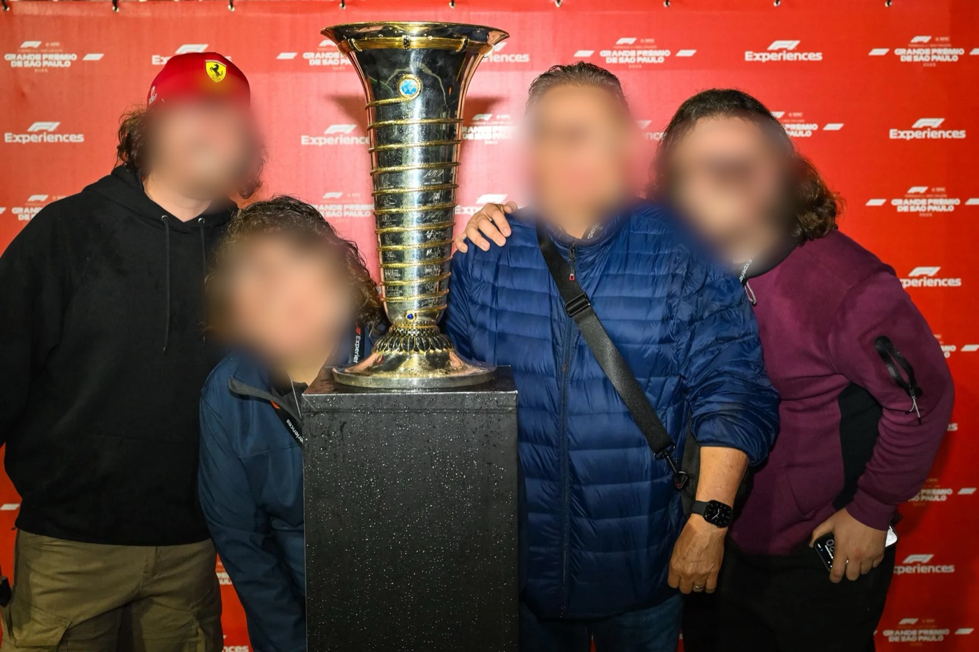 Cuatro visitantes posando junto al trofeo del Campeonato Mundial de Fórmula 1, frente a un fondo rojo de F1 Experiences. Las caras están difuminadas
