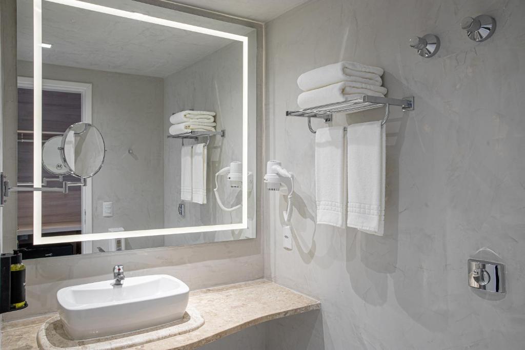 Baño de la habitación: lavatorio sobre mesada de mármol, espejo con luz, secador de pelo y toallas blancas